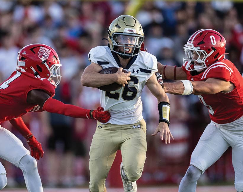 Three people in football uniforms are on a field with one person in a white and gold uniform running while two others in red uniforms attempt to block or tackle. Description generated by AI