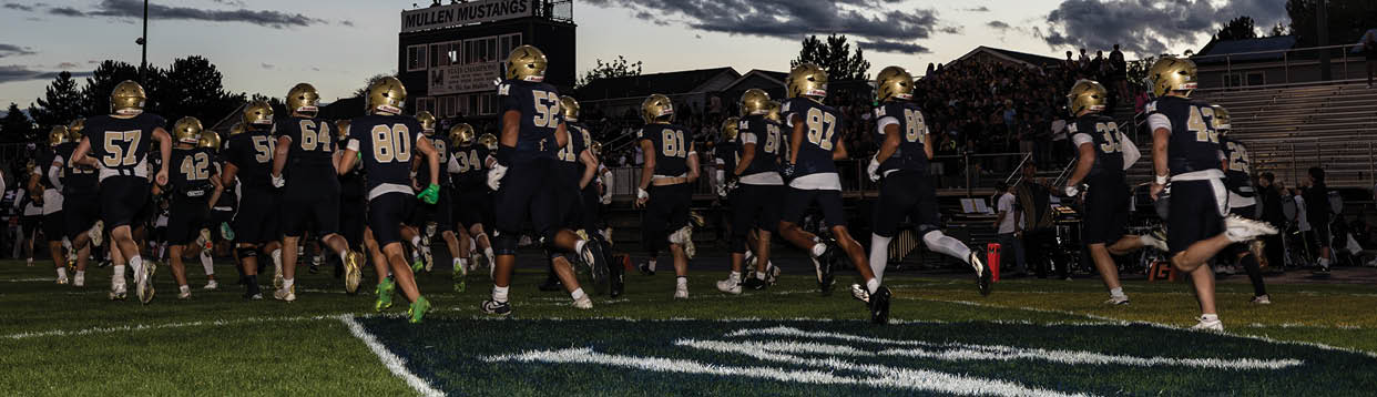 A group of people wearing dark sports uniforms and gold helmets are running together on a grassy field during dusk. Description generated by AI