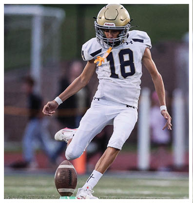 A person wearing a white football uniform is kicking a football on a field during a game. Description generated by AI