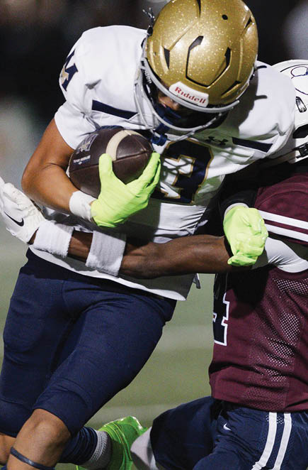 A person wearing a white shirt and navy blue pants is holding a football tightly while running on a field. Description generated by AI