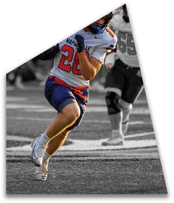 A person wearing a black football uniform and helmet is holding a football and appears to be preparing to run on a brightly lit field with blurred players in the background. Description generated by AI