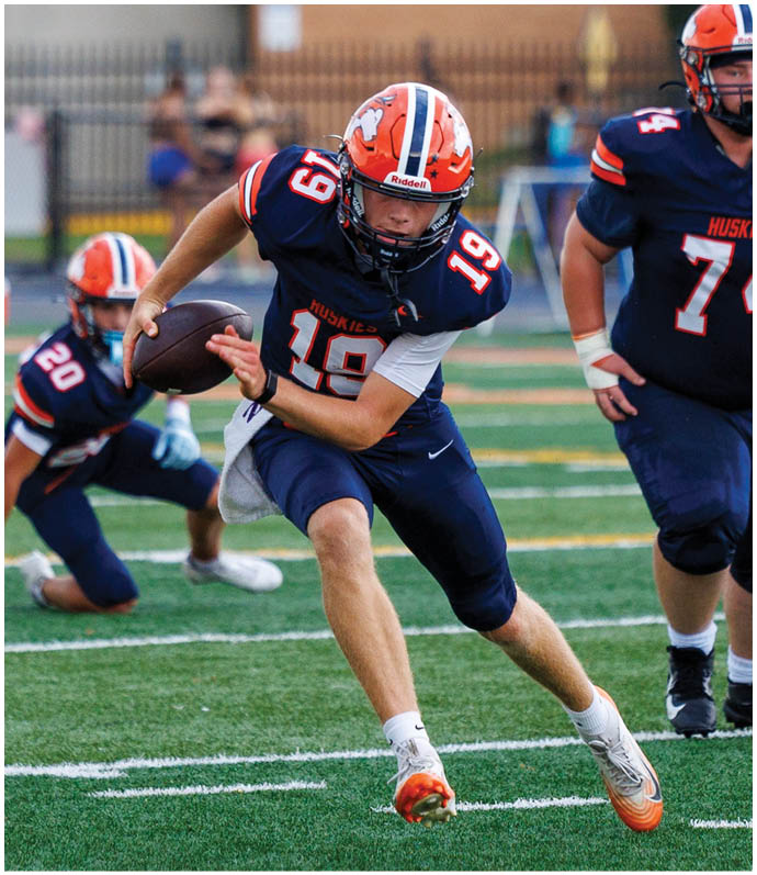 Three football players in blue and white uniforms running on a field. Description generated by AI