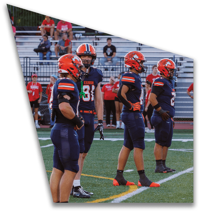 Two people in black football uniforms are engaged in a handoff with a football on a green field. Description generated by AI