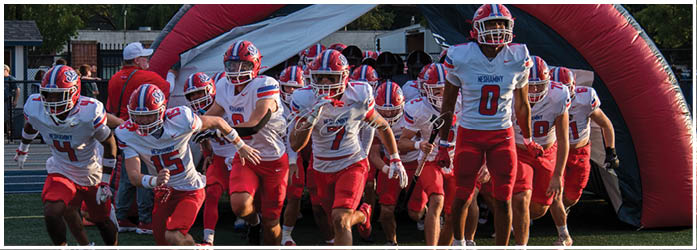 A group of people wearing red and white football uniforms are running out from an inflatable tunnel onto a field. Description generated by AI