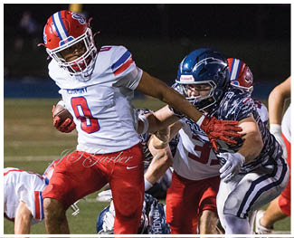 People wearing football uniforms are engaged in a physical play on a field during a game at night. Description generated by AI