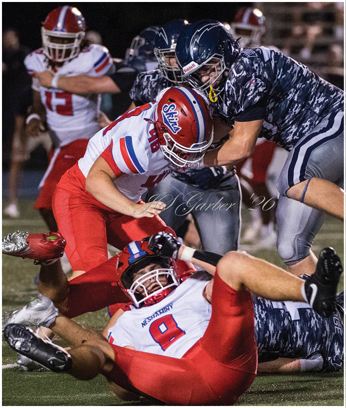 Several people wearing football uniforms are engaged in a dynamic play on a field during a nighttime game. Description generated by AI