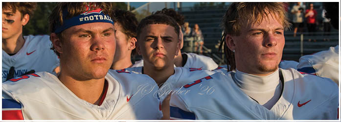 Two people wearing white football jerseys with “Neshaminy" written on them stand closely together, appearing focused and serious. Description generated by AI