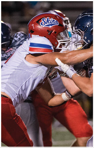 Two people in football uniforms and helmets are engaged in a close physical confrontation on a field during a game. Description generated by AI