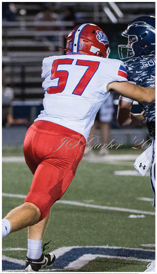 A person wearing a red and white football uniform with the number 57 is running on a football field. Description generated by AI