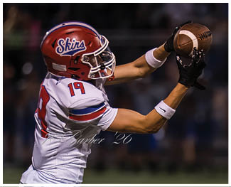 People wearing football uniforms are engaged in a physical play on a field during a game at night. Description generated by AI