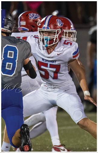 Two people in football uniforms and helmets are engaged in a close physical confrontation on a field during a game. Description generated by AI