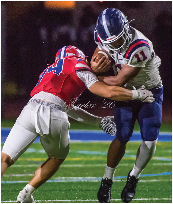 Several people wearing football uniforms are engaged in a dynamic play on a field during a nighttime game. Description generated by AI