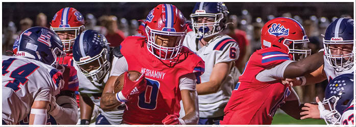 Two people wearing white football jerseys with “Neshaminy" written on them stand closely together, appearing focused and serious. Description generated by AI