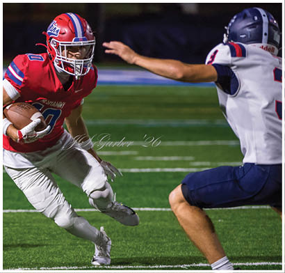Several people wearing football helmets and uniforms are actively engaged in a play on a football field at night. Description generated by AI