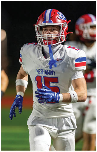 People wearing football uniforms are actively engaged in a play on a field, with one person in a dark blue and white uniform running while others in red and white uniforms attempt to catch them. Description generated by AI