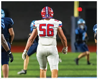 People wearing football uniforms are engaged in a physical play on a field during a game at night. Description generated by AI