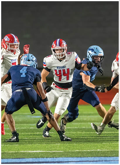 A group of people wearing red and white football uniforms are actively playing on a field, with one person holding the ball and running while others surround them. Description generated by AI