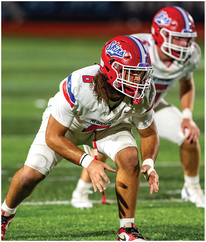 Three people in football uniforms are engaged in a play on a field, with one person holding the ball and another blocking an opponent. Description generated by AI