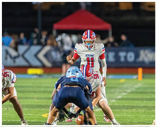 People wearing football uniforms are engaged in a physical play on a field during a game at night. Description generated by AI