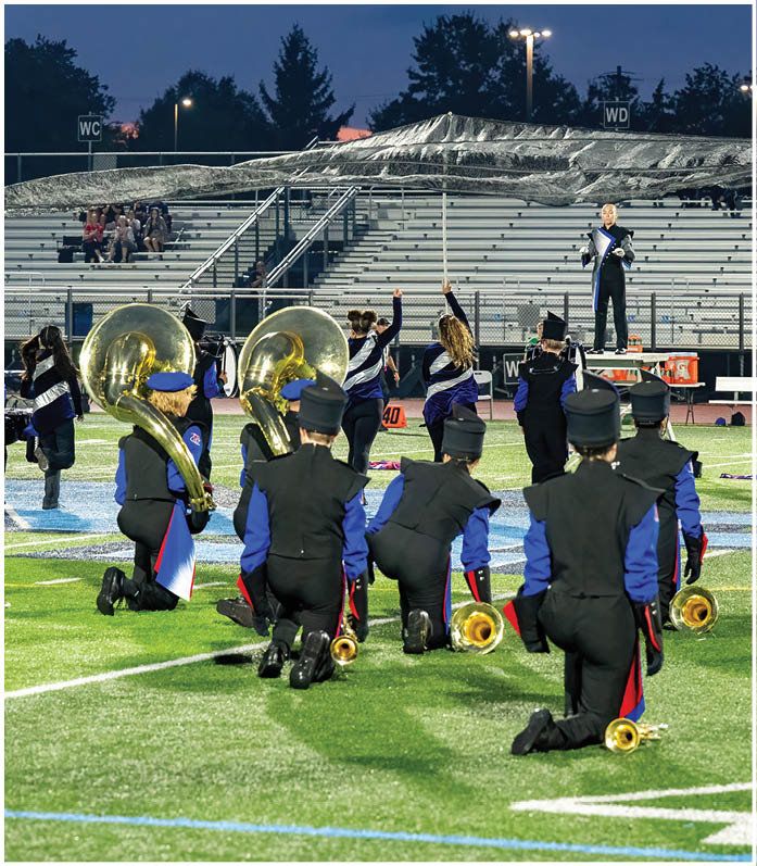 Three people in football uniforms are engaged in a play on a field, with one person holding the ball and another blocking an opponent. Description generated by AI