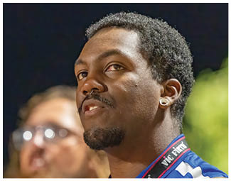 People wearing football uniforms are engaged in a physical play on a field during a game at night. Description generated by AI