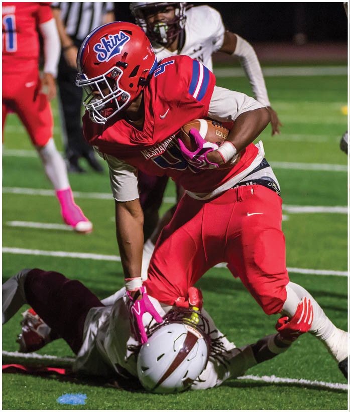 Three people in football uniforms are engaged in a play on a field, with one person holding the ball and another blocking an opponent. Description generated by AI