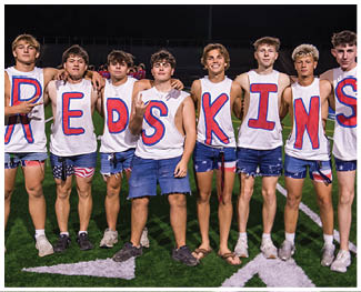 People wearing football uniforms are engaged in a physical play on a field during a game at night. Description generated by AI