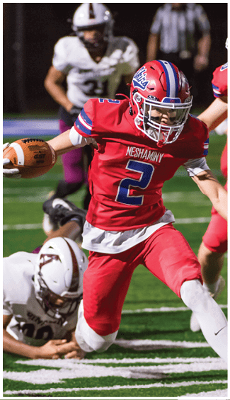 Two people in football uniforms are engaged in a physical play during a game, with one wearing a camouflage-patterned jersey and the other in a white and red uniform. Description generated by AI