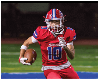 People wearing football uniforms are engaged in a physical play on a field during a game at night. Description generated by AI