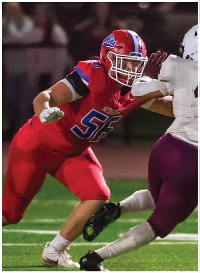 A group of people wearing red and white football uniforms are actively playing on a field, with one person holding the ball and running while others surround them. Description generated by AI