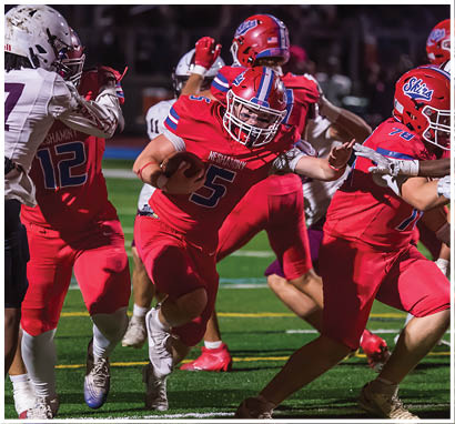 A line of people wearing red and white football uniforms and helmets are shaking hands on a football field at night with a crowd in the stands behind them. Description generated by AI