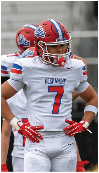 Two people in football uniforms are engaged in a physical play during a game, with one wearing a camouflage-patterned jersey and the other in a white and red uniform. Description generated by AI