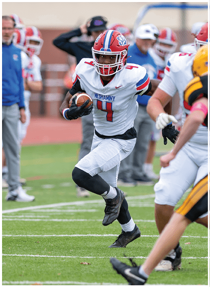 A group of people wearing red and white football uniforms are actively playing on a field, with one person holding the ball and running while others surround them. Description generated by AI
