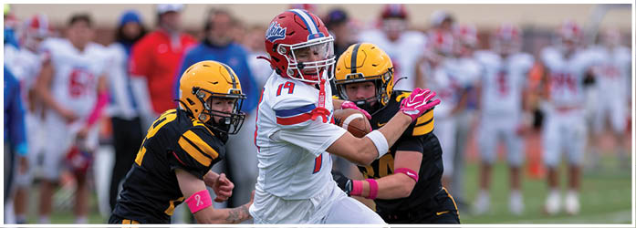 A group of people wearing red and white football uniforms are running out from an inflatable tunnel onto a field. Description generated by AI