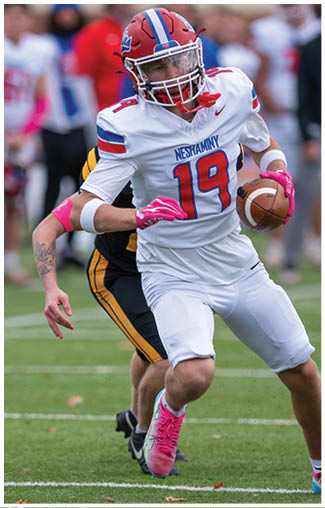 People wearing football uniforms are actively engaged in a play on a field, with one person in a dark blue and white uniform running while others in red and white uniforms attempt to catch them. Description generated by AI