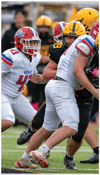 Two people in football uniforms are engaged in a physical play during a game, with one wearing a camouflage-patterned jersey and the other in a white and red uniform. Description generated by AI