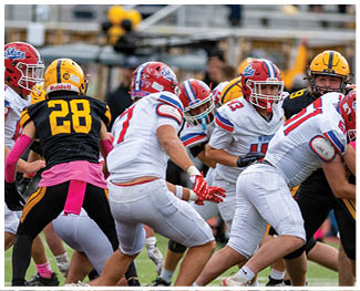 People wearing football uniforms are engaged in a physical play on a field during a game at night. Description generated by AI