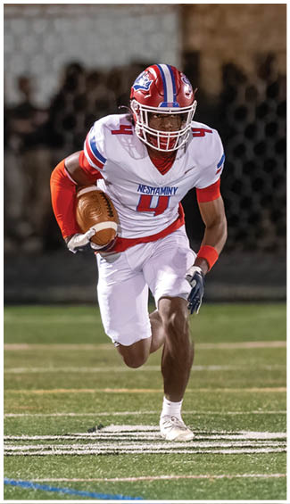 Two people in football uniforms are engaged in a physical play during a game, with one wearing a camouflage-patterned jersey and the other in a white and red uniform. Description generated by AI