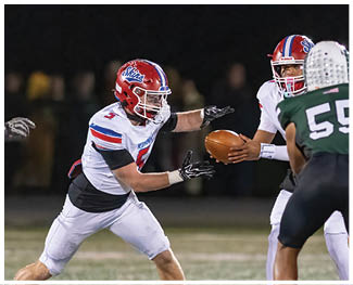 People wearing football uniforms are engaged in a physical play on a field during a game at night. Description generated by AI
