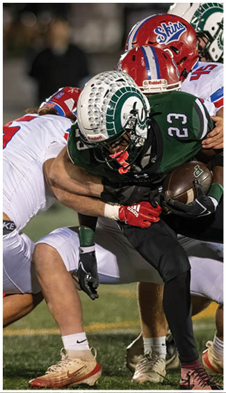 Two people in football uniforms are engaged in a physical play during a game, with one wearing a camouflage-patterned jersey and the other in a white and red uniform. Description generated by AI