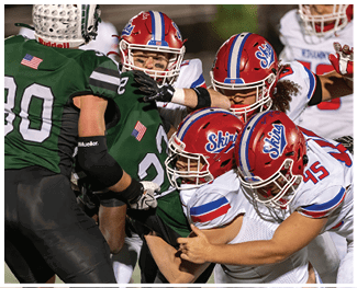 People wearing football uniforms are engaged in a physical play on a field during a game at night. Description generated by AI