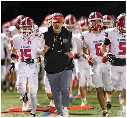 A line of people wearing red and white football uniforms and helmets are shaking hands on a football field at night with a crowd in the stands behind them. Description generated by AI