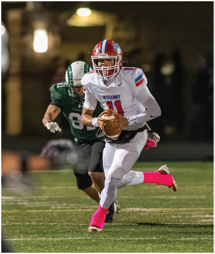 Three people in football uniforms are engaged in a play on a field, with one person holding the ball and another blocking an opponent. Description generated by AI
