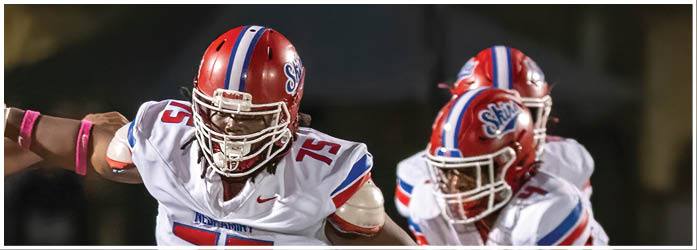 A group of people wearing red and white football uniforms are running out from an inflatable tunnel onto a field. Description generated by AI