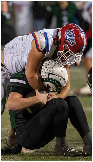 Two people in football uniforms are engaged in a physical play during a game, with one wearing a camouflage-patterned jersey and the other in a white and red uniform. Description generated by AI