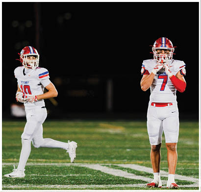 Several people wearing football helmets and uniforms are actively engaged in a play on a football field at night. Description generated by AI