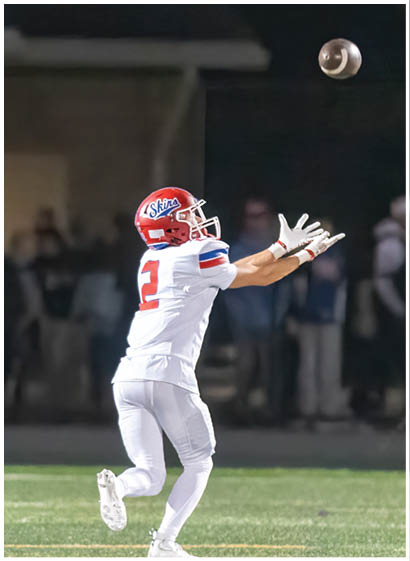 A group of people wearing red and white football uniforms are actively playing on a field, with one person holding the ball and running while others surround them. Description generated by AI