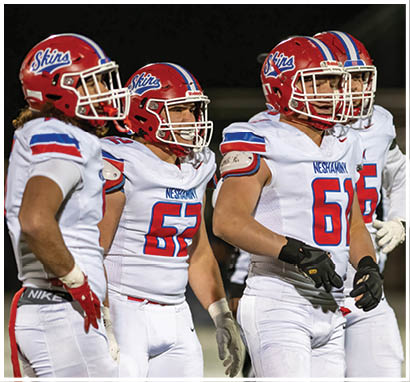 A line of people wearing red and white football uniforms and helmets are shaking hands on a football field at night with a crowd in the stands behind them. Description generated by AI