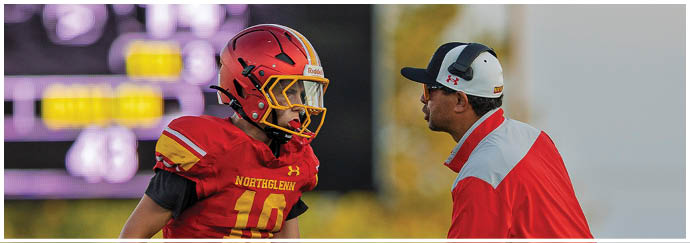 A football player wearing a red and yellow jersey shakes hands with a man in a red shirt. Description generated by AI
