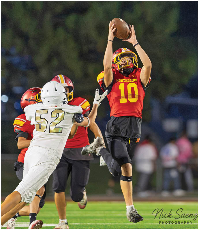 A football player in a red and yellow jersey catching a football. Description generated by AI